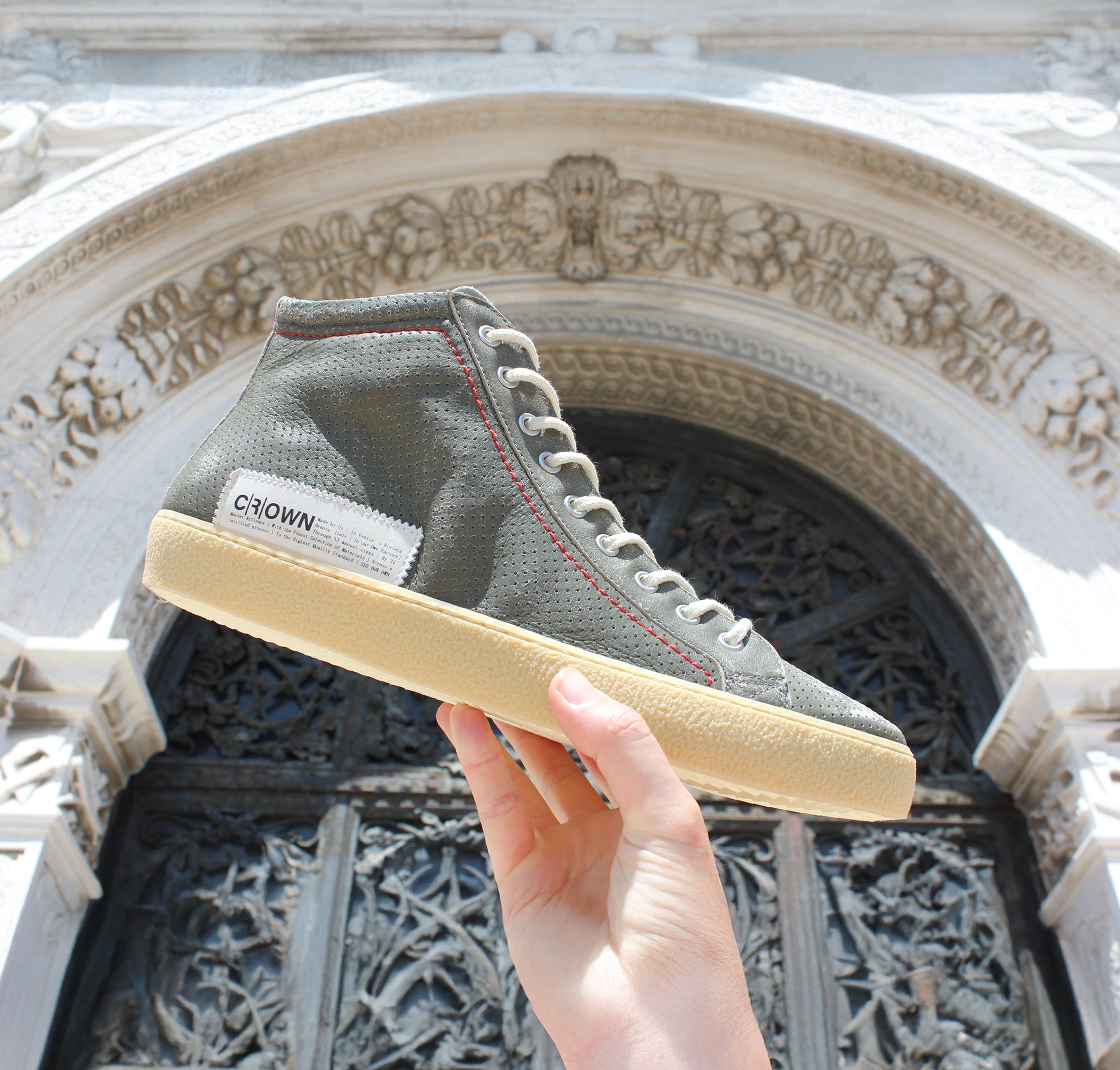 Perforated khaki high-top sneaker being held up by a hand